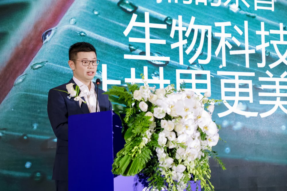 A person standing at a podium with flowersDescription automatically generated A person standing at a podium with flowersDescription automatically generated